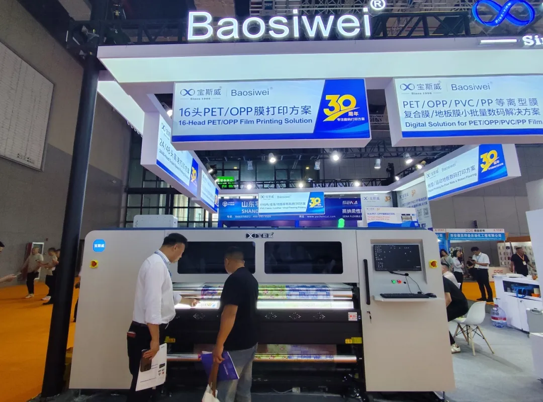 Two Baoswei technicians operating 16-head PET OPP film industrial digital printer at DOMOTEX Asia — no plate-making direct-to-film production