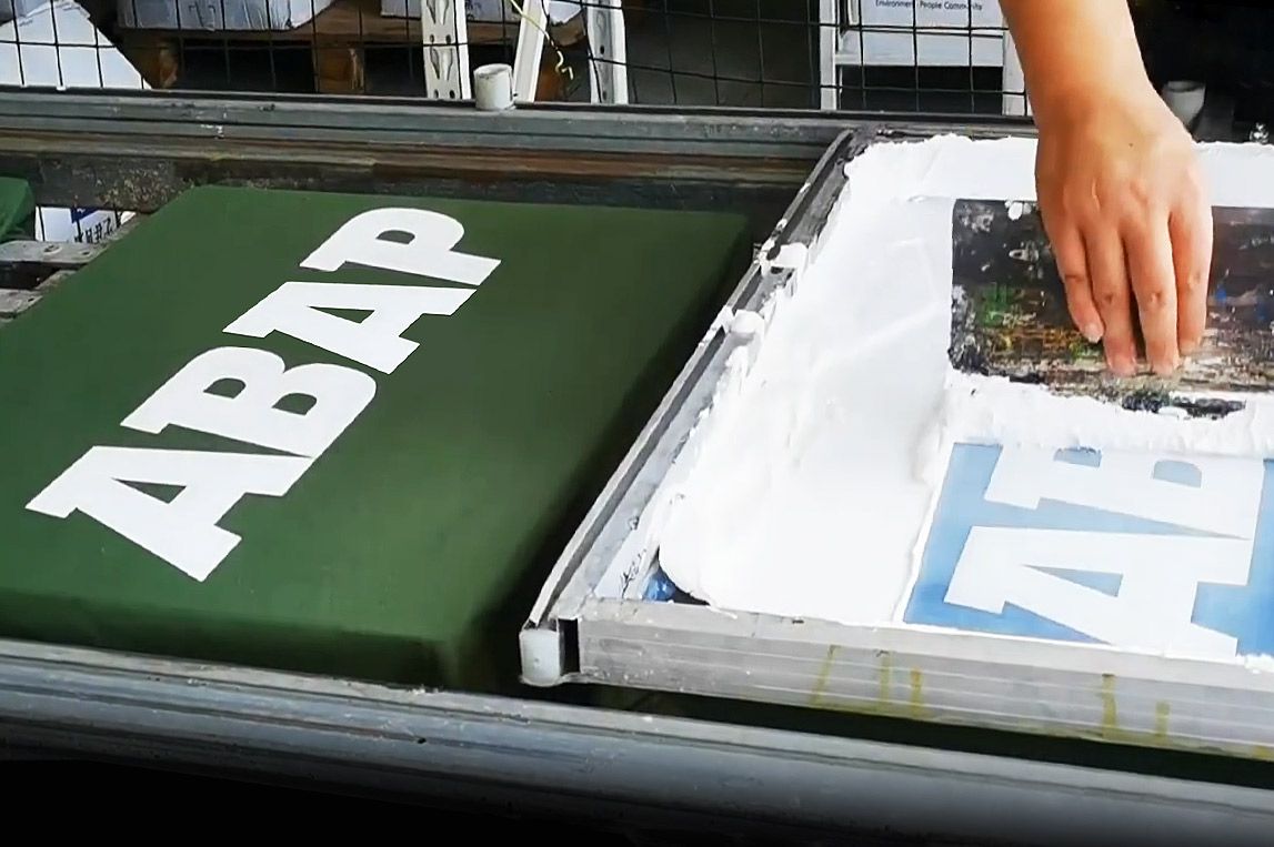 Worker using a squeegee to press ink onto fabric, screen printing English letters on a garment