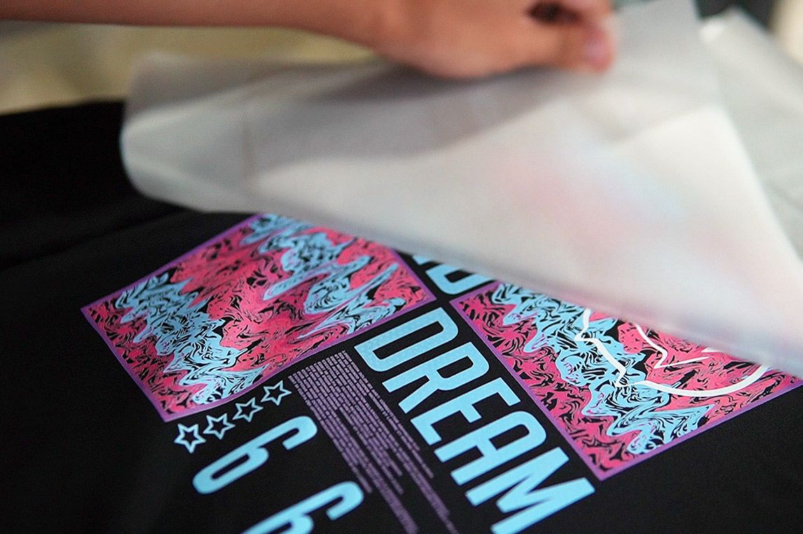 Worker peeling off DTF transfer film after heat pressing a design printed by Baosiwei DTF printer, demonstrating digital transfer printing with easy peel and sharp graphics, ideal for custom T-shirts, garment decoration, and textile printing.
