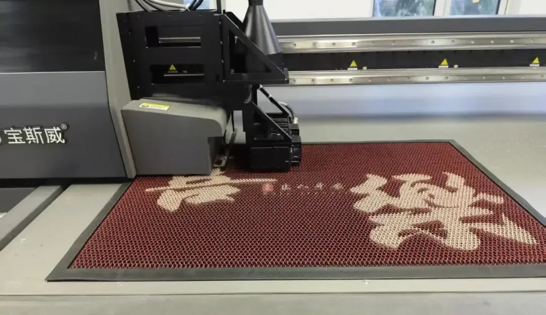 Baosiwei 2513 UV flatbed printer in operation, printing patterned designs on a red-mesh floor mat material—showcasing the device’s mat printing application.