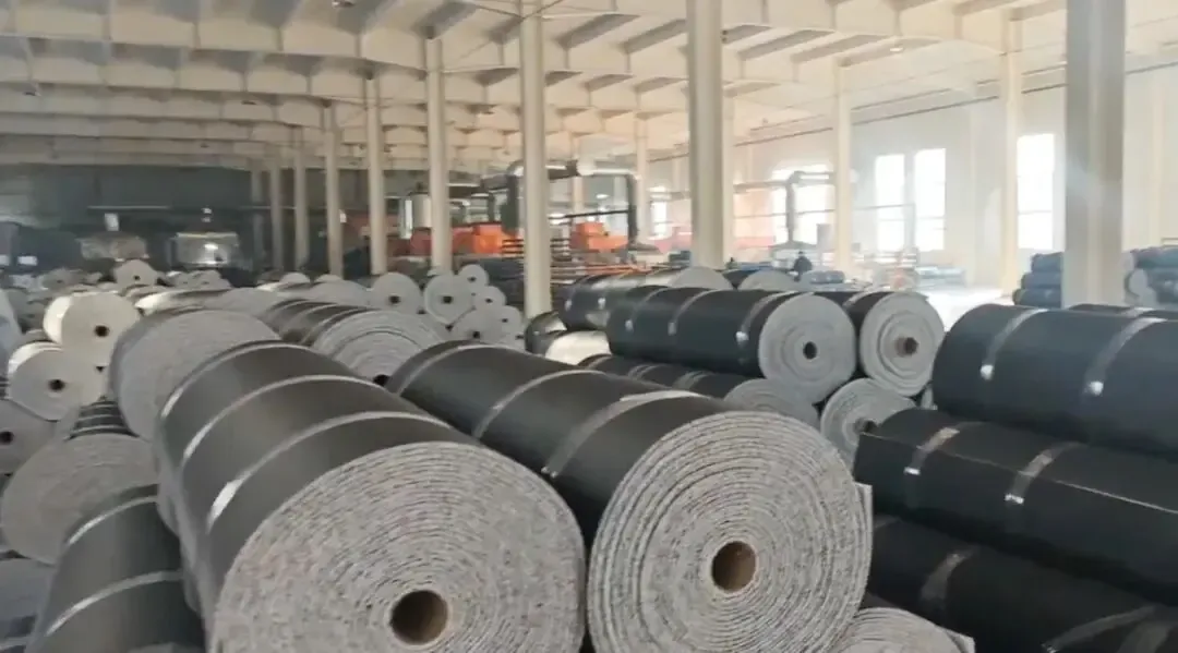 Floor mat factory workshop with stacks of gray and black floor mat base material rolls — these are raw materials prepared for subsequent printing and processing.